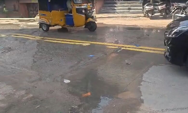 Street scene with auto rickshaw, motorcycles, and cars on a wet road in India.