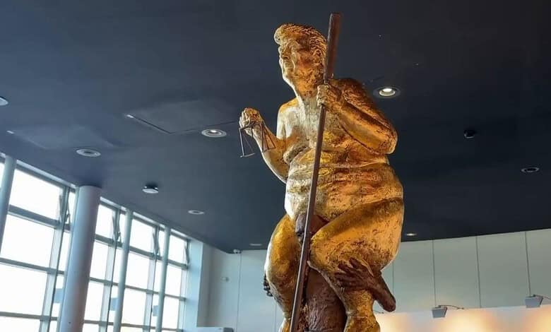 Golden statue of a woman holding a staff, displayed indoors with large windows in the background.