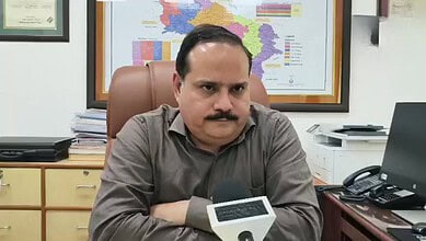 UP CEO seated at desk with map of India in background, serious expression.