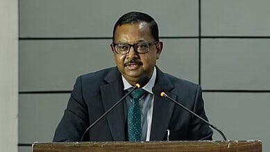 Man in suit speaking at a podium during a formal event or press conference.