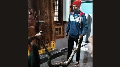 Man holding a large snake inside a traditional wooden room in Telangana.