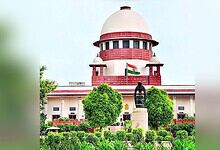 Supreme Court of India building with Indian flag and lush greenery in front.