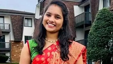 Smiling woman in traditional Indian saree outdoors in front of residential buildings.