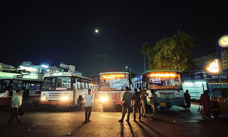 Nighttime scene at a bus station with multiple buses and people under a dark sky.
