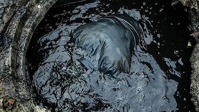 Man in black clothing working in a dark, polluted manhole for manual scavenging.
