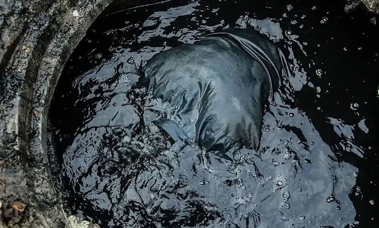 Man in black clothing working in a dark, polluted manhole for manual scavenging.