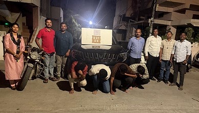 Group of people standing and kneeling in front of a vehicle at night.