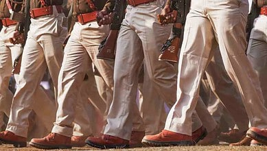 Group of uniformed personnel walking in formation, holding rifles, in an outdoor setting.