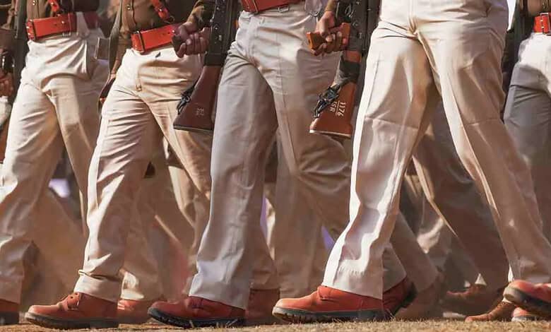 Group of uniformed personnel walking in formation, holding rifles, in an outdoor setting.