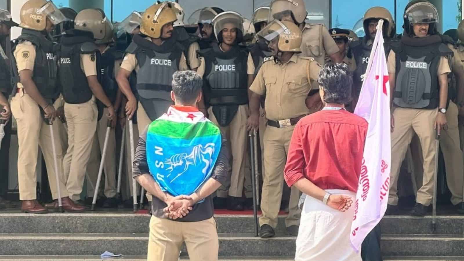 Protest at Central University of Kerala with police in riot gear and students holding flags.