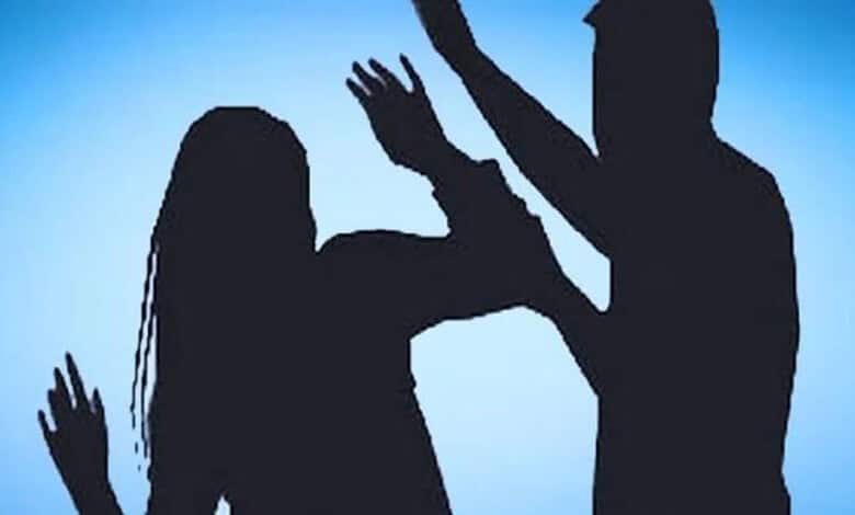 Silhouette of a man hitting a woman during a confrontation against a blue background.