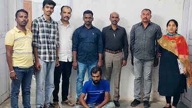 Group of eight diverse individuals standing indoors, one seated in front, in a professional setting.