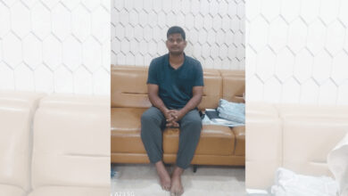 Young man sitting on a brown sofa in a modern room with white hexagonal wall tiles.