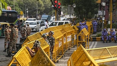 Security personnel and protesters behind yellow barricades at a busy intersection in Delhi.