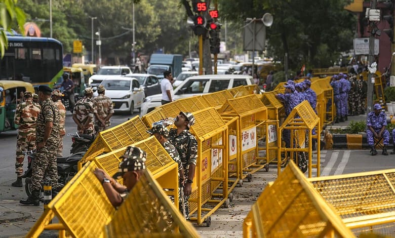 Security personnel and protesters behind yellow barricades at a busy intersection in Delhi.