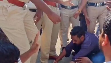 Man kneeling on the ground pleading with police officers in a crowd during a protest.