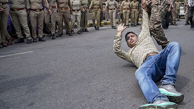 Protester falling on the road during a demonstration in Delhi with police in the background.