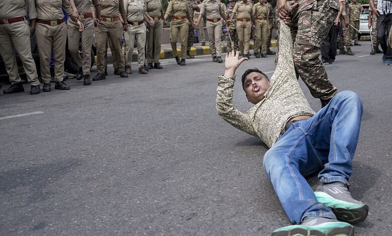 Protester falling on the road during a demonstration in Delhi with police in the background.