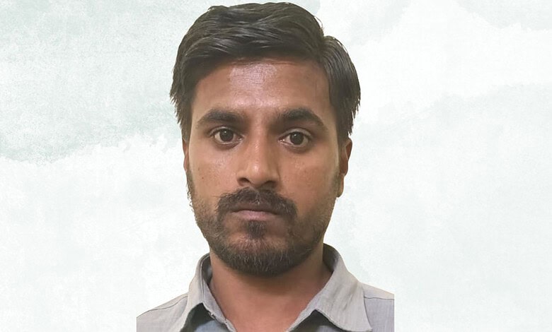 Close-up of a young man with dark hair and beard looking serious against a light background.