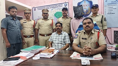 Police officers and a man seated at a desk in Chadeghat police station, Hyderabad City.