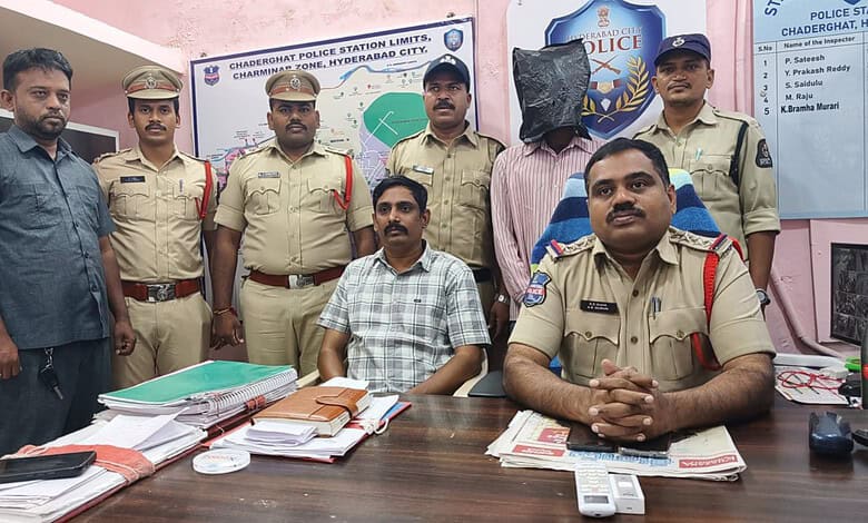 Police officers and a man seated at a desk in Chadeghat police station, Hyderabad City.