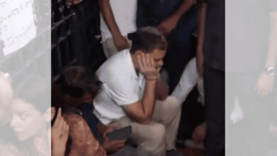 Man sitting on the ground with hand on face, surrounded by people at a protest or gathering.
