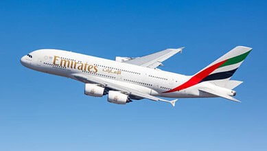 Emirates airplane flying in clear blue sky, showcasing airline branding and design.