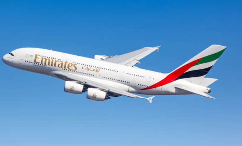 Emirates airplane flying in clear blue sky, showcasing airline branding and design.