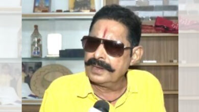 Man with moustache wearing sunglasses and yellow shirt in an indoor setting.