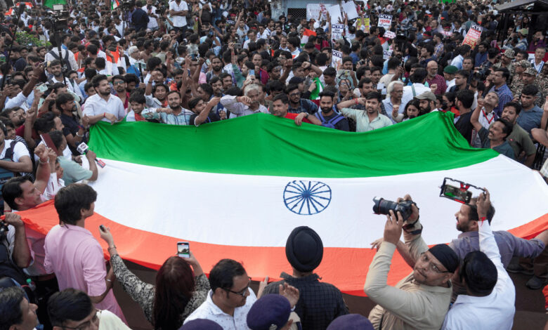 Large crowd holding a giant Indian flag during a protest rally in Delhi.