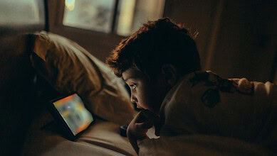 Young boy watching a tablet screen in a dimly lit room at night.