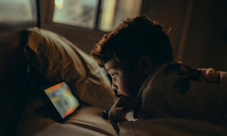 Young boy watching a tablet screen in a dimly lit room at night.