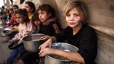 Children in Gaza waiting for aid, some holding bowls, in a distressing scene.