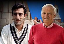 Two men, a young and an elderly, standing outdoors with a historic building in the background.