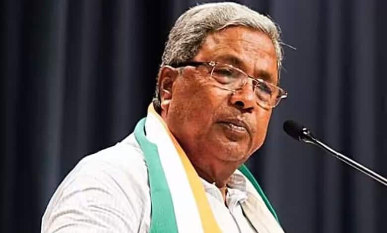 Former CM Siddaramaiah speaking at a press conference with a microphone and a dark background.
