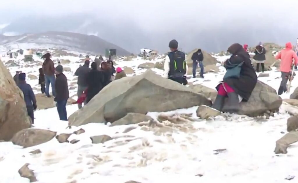 Tourists and visitors enjoy snowfall in the high reaches of Kashmir amid snowy rocks and cloudy skies.
