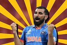 Indian cricket player celebrating with fists raised, wearing blue jersey with 'India' logo.