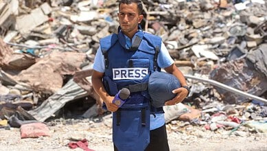 Gaza journalist Anas Al-Sharif in front of rubble after an attack.