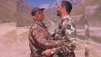 Two soldiers in camouflage uniforms sharing a moment in a mountainous landscape.