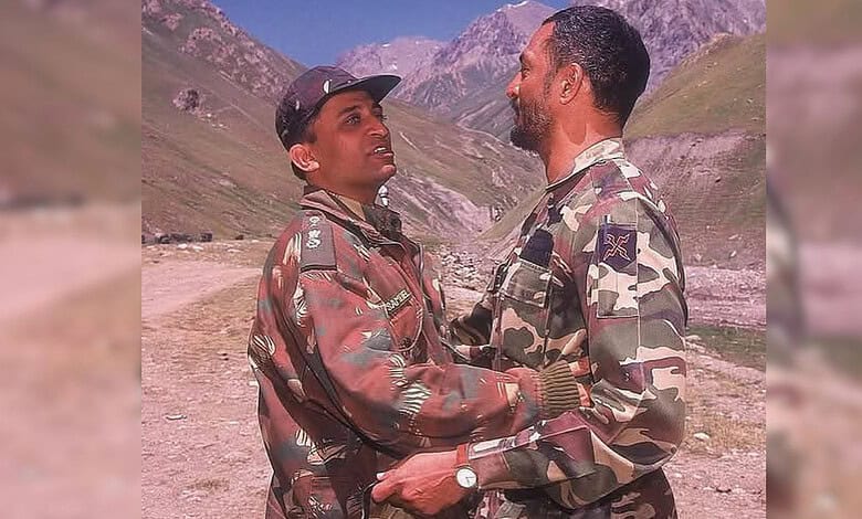 Two soldiers in camouflage uniforms sharing a moment in a mountainous landscape.