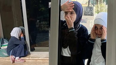 Girls wearing headscarves look out from school window, appearing worried and anxious.