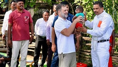 Man in white uniform hands over a gift to a smiling man holding a child in an outdoor setting.