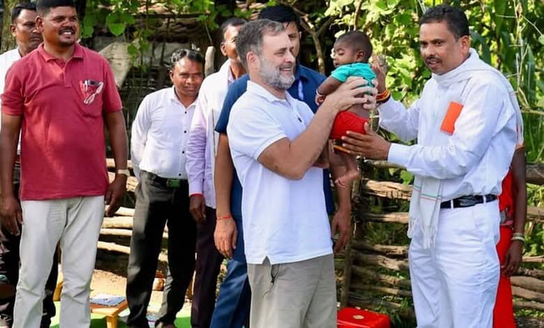 Man in white uniform hands over a gift to a smiling man holding a child in an outdoor setting.