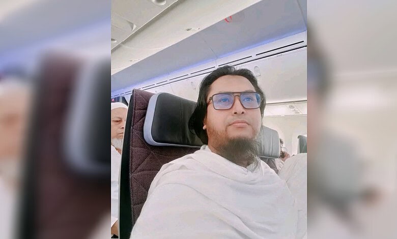 Man with glasses sitting on an airplane, wearing a white shawl, looking forward.