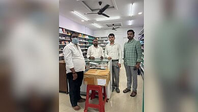 Four men in a store, one wearing a face mask, standing around a glass display case.