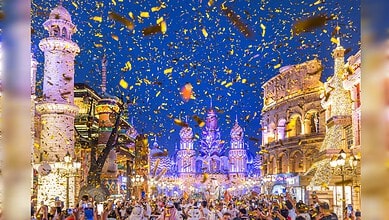 Crowd celebrating at Dubai Global Village with fireworks and confetti in the night sky.