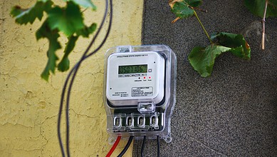 Electricity meter on a wall with green leaves nearby, showing a reading of 950716.