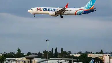 Flydubai plane flying in cloudy sky with cityscape below.