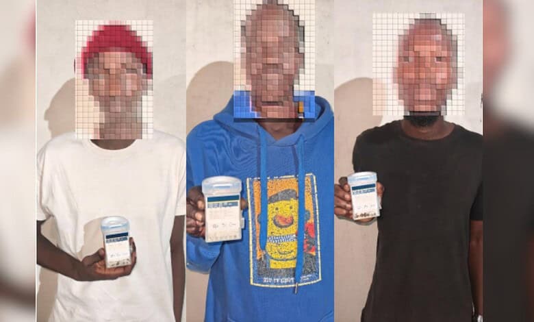 Three men holding mobile phones, image pixelated, in front of a plain background.