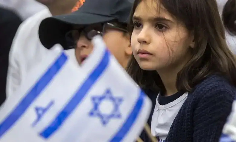 Young girl with serious expression holding an Israeli flag at a public event.